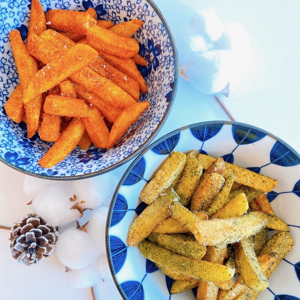 Two blue-and-white bowls of seasoned fries, one orange with a spice dusting and one green-flecked.