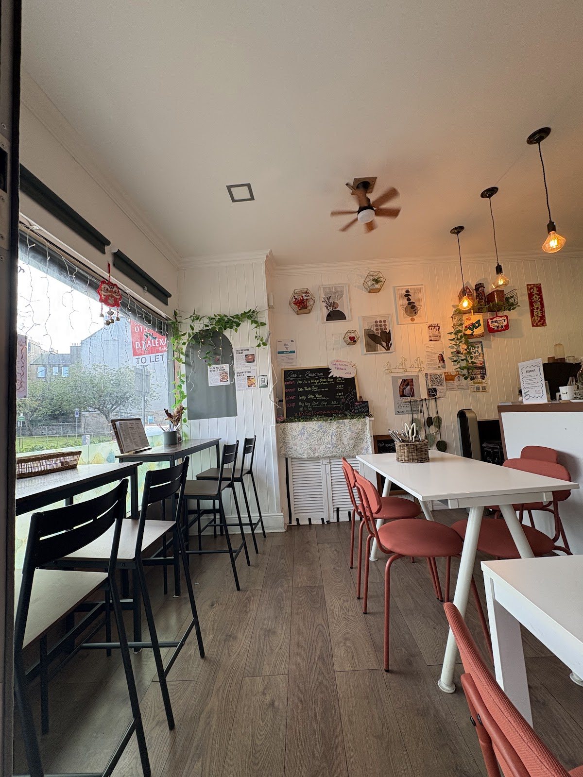 Inside No Boundary: white walls with small framed prints, pendant lights and a ceiling fan, terracotta chairs at white tables, and high stools at the window counter.