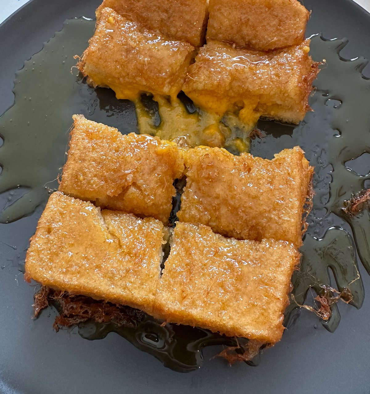 Hong Kong French toast: thick golden fried slices cut into squares, filled and glistening with syrup, on a slate-grey plate.